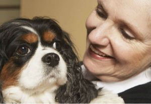 An elderly woman holds a Cocker Spaniel dog and smiles down lovingly at it.