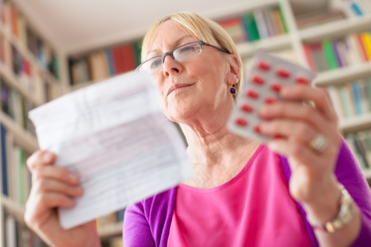 An elderly woman holds medical paperwork and medication in her hands.