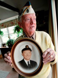 An elderly Pearl Harbor veteran holds an old photo of his younger self in service.