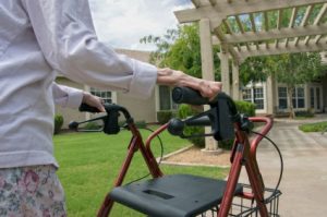 An elderly woman with a walker approaches her front door to her home.