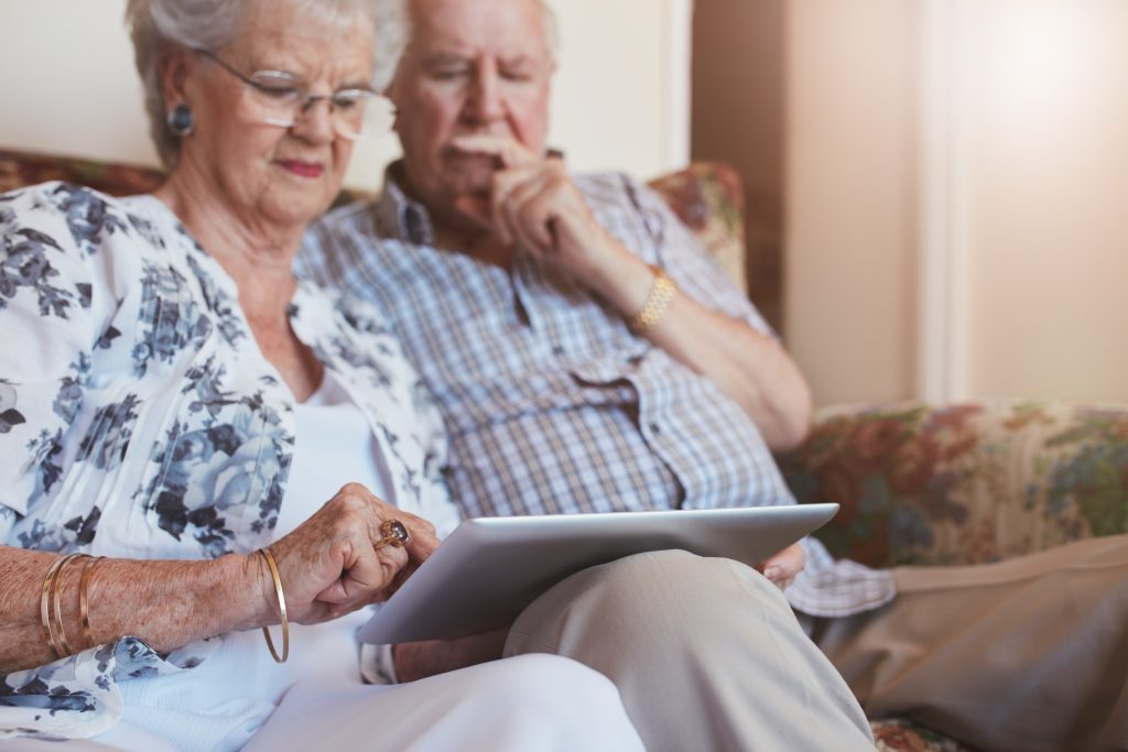 Portrait of elderly woman sitting with her husband and using digital tablet. Retired couple sitting on sofa at home with a touch screen computer.