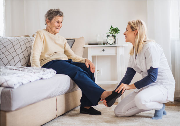 A health visitor putting on slippers on a senior woman at home