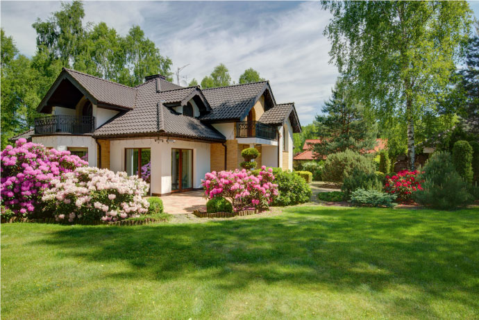 Big house in suburban neighborhood with green lawn, flowers, bushes, and trees