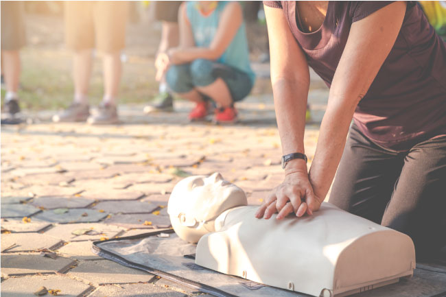 Candid of mature asian female or older runner woman training on CPR demonstrating class in outdoor park and put hands over CPR doll on chest.