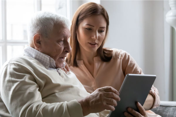 young female caregiver showing elderly man tablet