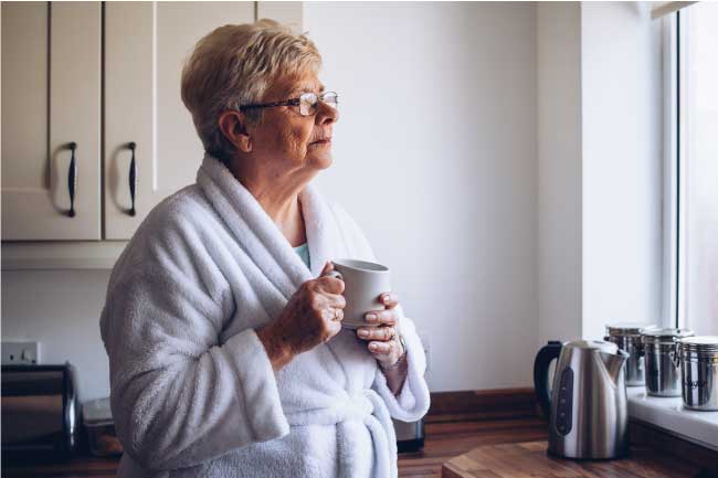 Elderly woman in her kitchen at home alone looking out of the window. daily call depression