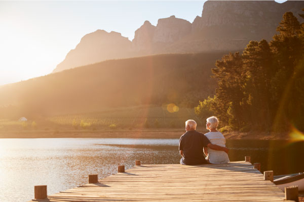 Romantic-Senior-Couple-Sitting-On-Wooden-Jetty-By-Lake
