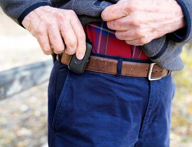 elderly man using bay alarm medical sos mobile gps device on belt clip